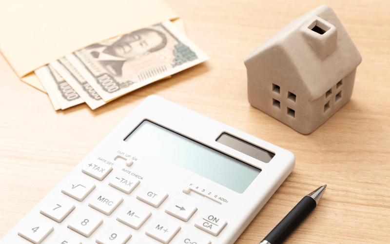 住宅ローンや費用の話。電卓とお金が家の模型と一緒に置いてある