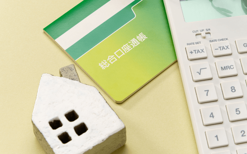 通帳・電卓・家の置物が並ぶ、相続手続きのお金をイメージした写真